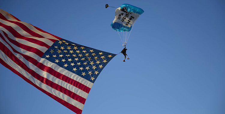 A veteran wearing a parachute is presenting the American flag falling from the sky.